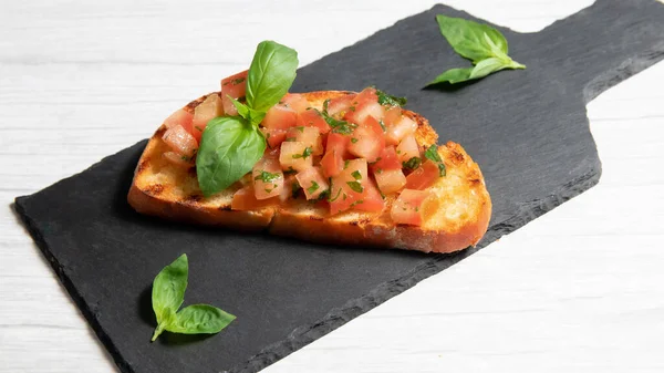 Siyah tabakta bruschetta, beyaz ahşap arka planda.