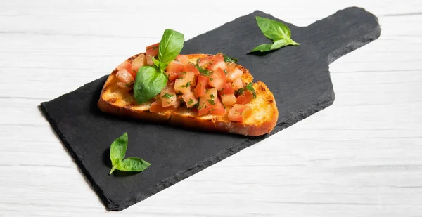 Siyah tabakta bruschetta, beyaz ahşap arka planda.