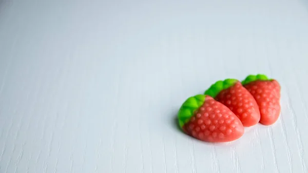 Drie Aardbeien Gummies Een Witte Tafel Met Groen Blad — Stockfoto