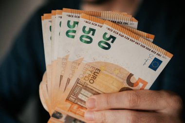 Avro banknotlarını elinde tutan bir adamın yakın çekimi.