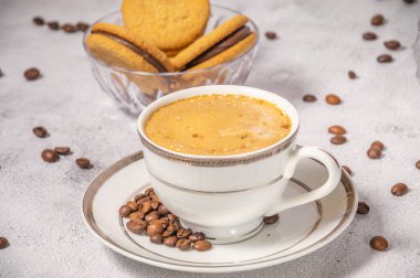 Kahve fincanı, kahve çekirdekleri ve tatlılar arka planda.