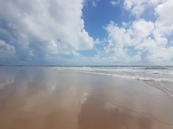 雲の間の青い空の下の砂を覆う水の海 — ストック写真