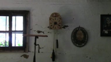 Eski ahşap bir evin içi: sarkaçlı bir saat karanlık bir odanın beyaz duvarında asılı, ikonlu bir resim.