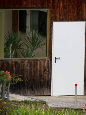 Metal kapılı ahşap duvar. Palmiye ağaçlı büyük pencere.