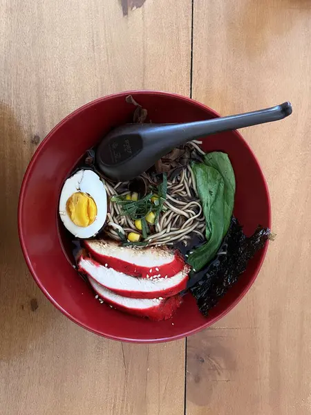 Ahşap masada kırmızı kasede bir shoyu ramen. Geleneksel Japon erişte çorbası tavuk, nori ve yumurta.