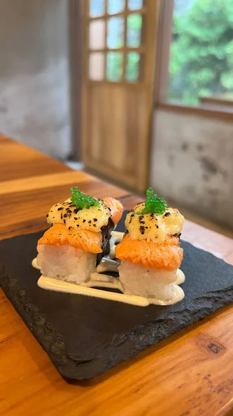 Estetik tabakta servis edilen krem peynirli somon Nigiri Sushi. Tahta masa ve bulanık arkaplan