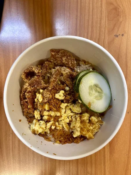 Üst açılı pirinç kasesi, çırpılmış yumurta, turşu dilimi ve çıtır tavuk derisi.