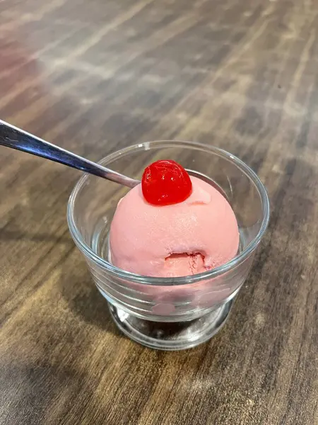 Üzerinde kiraz olan bir cam kasede çilekli dondurma.