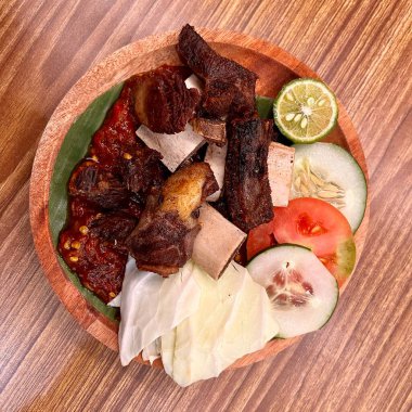 Biftek, kırmızı biber sosu, limon, turşu ve domatesli ahşap tabakta servis edilir.