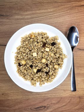 Tahta arka planda beyaz bir tabakta fındık ve kuru üzümlü granola. Üst Manzara. Sağlıklı bir kahvaltı..