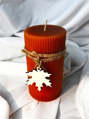 Flüt kenarlı turuncu mum ve beyaz bir tekstil arka planındaki ipliğe bağlı ahşap bir yaprak. Üst görünüm.