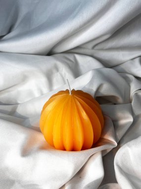 Beyaz tekstil arka planında balkabağı şeklinde turuncu mum. Üst görünüm.