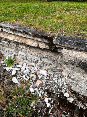 Eski yıkılmış tuğla bir çit yosun ve yabani çalılarla kaplıdır. Parktaki tahrip olmuş tuğla çit..