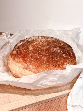 Taze pişmiş yuvarlak ekmek, ahşap bir masada, kağıt fırınında..