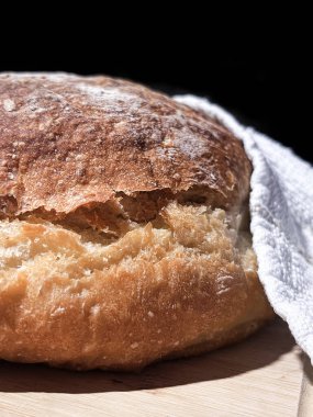 Ahşap bir tahtanın üzerinde siyah arka planı olan taze pişmiş yuvarlak ekmek. Kapat..