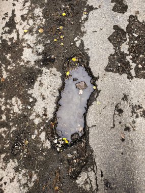 Yoğun asfalt yol yüzeyinde büyük bir çukur var. Asfalttaki çatlaklar yüzünden bir şehir caddesinde kaza olmuş. Çamurlu suyla dolu kırık bir delik..