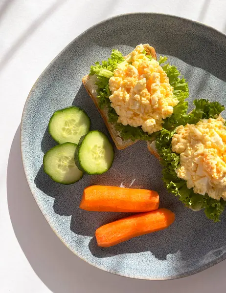 Beyaz arka planda gölgeli bir tabakta salatalıklı ve havuçlu yumurta salatalı sandviç. Sağlıklı kahvaltı.