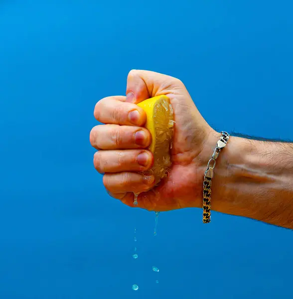 Mavi arka planda sarı sulu bir limonu sıkmak.