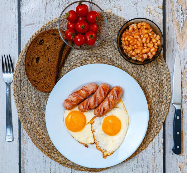 İngiliz kahvaltı yumurtası, sosis, domates, ekmek ve fasulye beyaz tabakta.