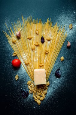 Koyu arkaplanda farklı türde makarna, un, peynir, domates, fesleğen, sarımsak, sanat