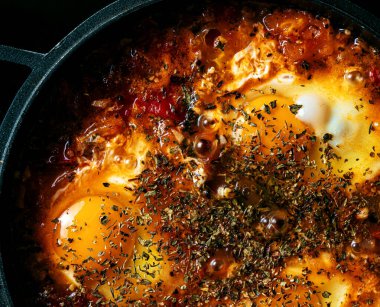 Shakshuka, siyah arka planda siyah bir tavada baharatlar.