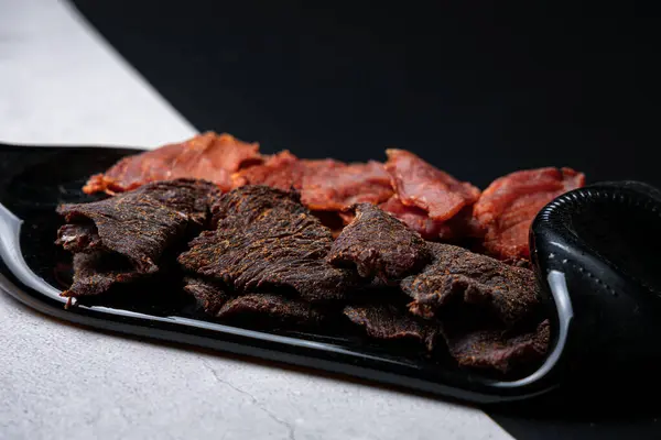 Bir tabakta kurutulmuş et atıştırmalıkları ve zıt bir arka planda izole edilmiş bir şişe şarap.