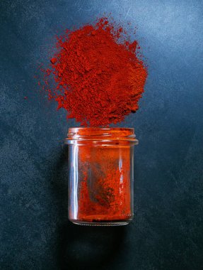 Kırmızı biber bir kavanozdan dökülüyor koyu bir arka plan sanatına izole edilmiş.