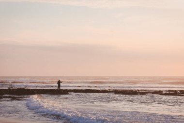 Portekiz 'in Vila Nova de Milfontes kasabasında Atlantik Okyanusu üzerinde insan ve günbatımı
