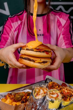 Elinde peynirli hamburger tutan bir kız.