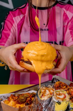 Elinde peynirli hamburger tutan bir kız.