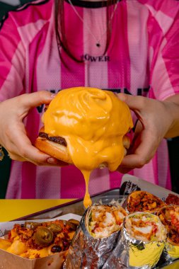 Elinde peynirli hamburger tutan bir kız.