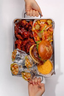 Elleri hamburger, shawarma ve patates kızartması ile bir sete uzanıyor.