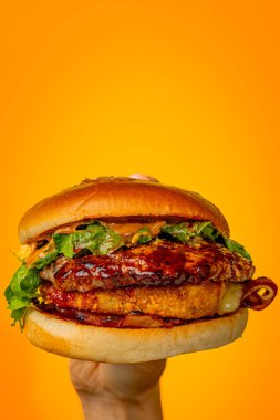 Turuncu bir arka planda parlak sulu bir burger tutuyor.