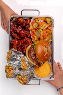 Elleri hamburger, shawarma ve patates kızartması ile bir sete uzanıyor.