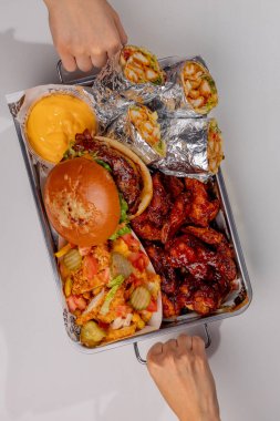 Elleri hamburger, shawarma ve patates kızartması ile bir sete uzanıyor.