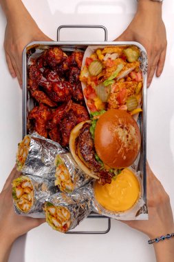 Elleri hamburger, shawarma ve patates kızartması ile bir sete uzanıyor.