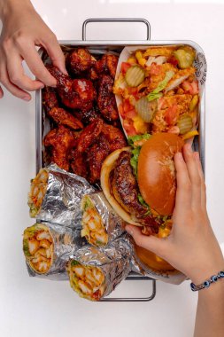 Elleri hamburger, shawarma ve patates kızartması ile bir sete uzanıyor.