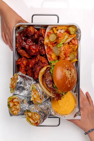 Elleri hamburger, shawarma ve patates kızartması ile bir sete uzanıyor.