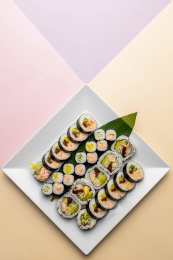 Suşi beyaz kare tabakta maki sarıyor.