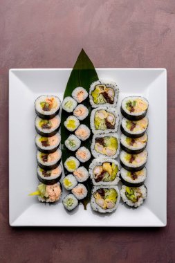 Suşi beyaz kare tabakta maki sarıyor.