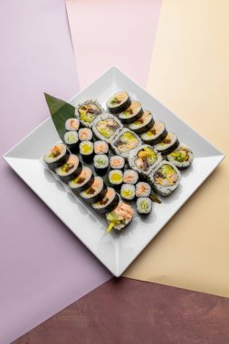 Suşi beyaz kare tabakta maki sarıyor.