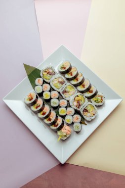 Suşi beyaz kare tabakta maki sarıyor.