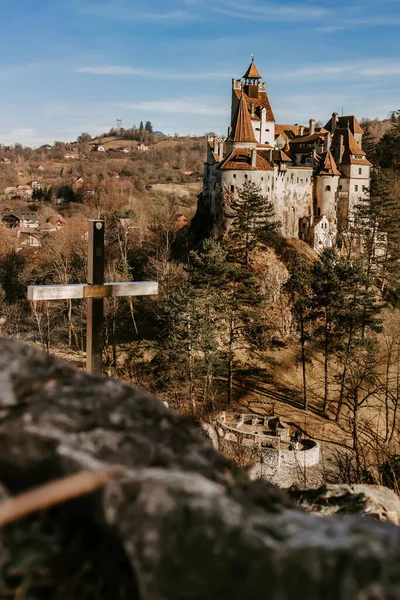Bran castle or Count Dracula Castle view from viewpoint on hill with cross. Medieval fortress in Romania, popular travel destination and touristic landmark. Gothic vampire castle in haunted forest.
