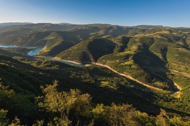 Meandering Zavoj lake landscape from Kozji Kamen viewpoint. Summer sunset at lake Zavojsko, panorama from viewing point Goat rock. River surrounded by wooded slopes of Stara planina National park.