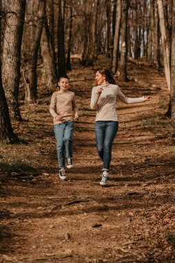 Ormanda koşan genç anne ve çocuk. Aktif aile güneşli bir günde doğada eğleniyor. Mutlu anne ve oğul oyun oynuyor ve birlikte dışarıda vakit geçiriyorlar..