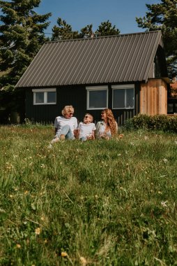 Yetişkin bir kızı ve torunu olan büyükanne kırsal alanda dinleniyor. Mutlu çoklu nesil aile, kır evlerinde çimlerin üzerinde oturup birlikte tatil yapıyorlar. Aile tatili kavramı.