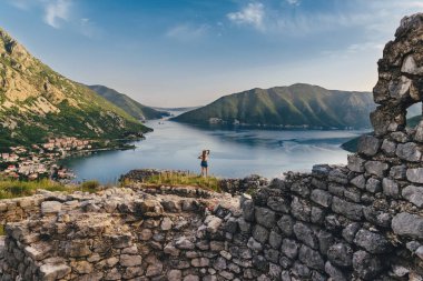 Eski İlirya kalesi Rizon 'un kalıntıları üzerinde duran kadın gezgin. Kotor Körfezi manzaralı bir kadın, Boka Kotorska 'nın Risan kasabasının yukarısındaki en eski yerleşim yerlerinden biri. Karadağ 'ı gezme kavramı.