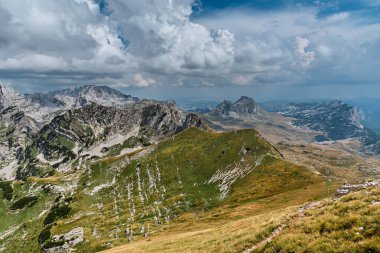 Karadağ 'ın Durmitor Ulusal Parkı' ndaki Dinaric Alp Dağları üzerinde dramatik bir gökyüzü bulunan dağ manzarası. Yeşil dağ vadisi ve dağ tepesinde yürüyüş yolu olan dağlık bir manzara..