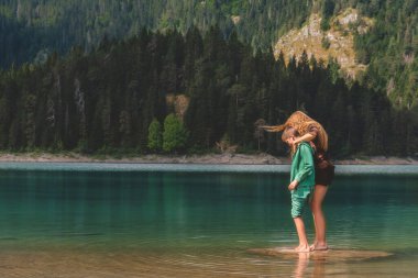 Güzel bir kadın, yaz mevsimi dağ gölünün ve yüksek dağlardaki kozalaklı ormanın arka planında oğluna sarılıyor. Anne ve çocuk Durmitor 'da doğa üzerinde boş vakitlerin tadını çıkarıyorlar. Karadağ.