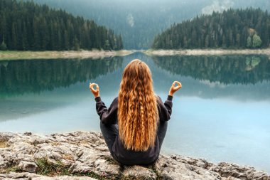 Dağ gölünün kıyısında meditasyon yapan bir kadın. Durmitor 'da Kara Göl' de sabah Yoga antrenmanı yapan bir kadın. Dişi yalnız gezgin sessizliğin ve yalnız kalmanın tadını çıkarıyor, sisli gölün manzarasını seyrediyor..